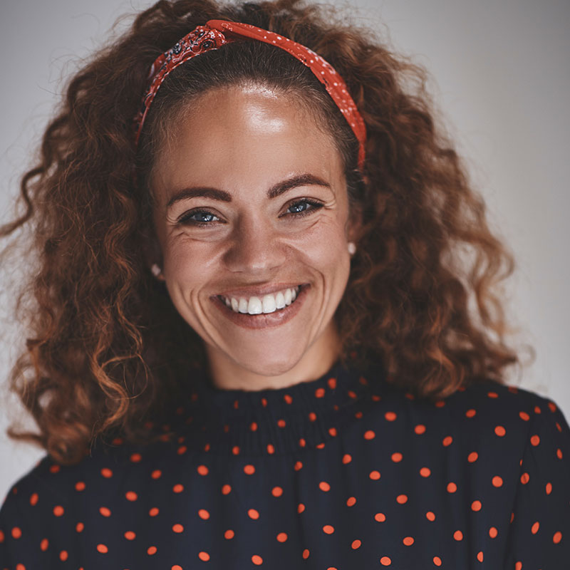 A woman with curly hair and a headband smiles.