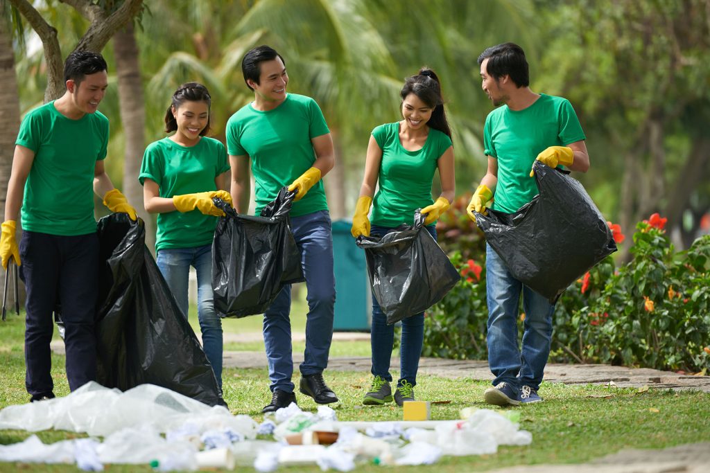 A group of people in green shirts holding garbage bags.