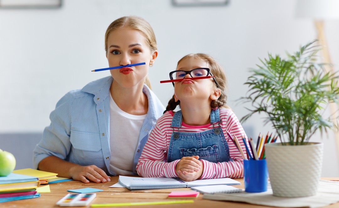 A woman and child sitting at a table with pencils in their mouths.