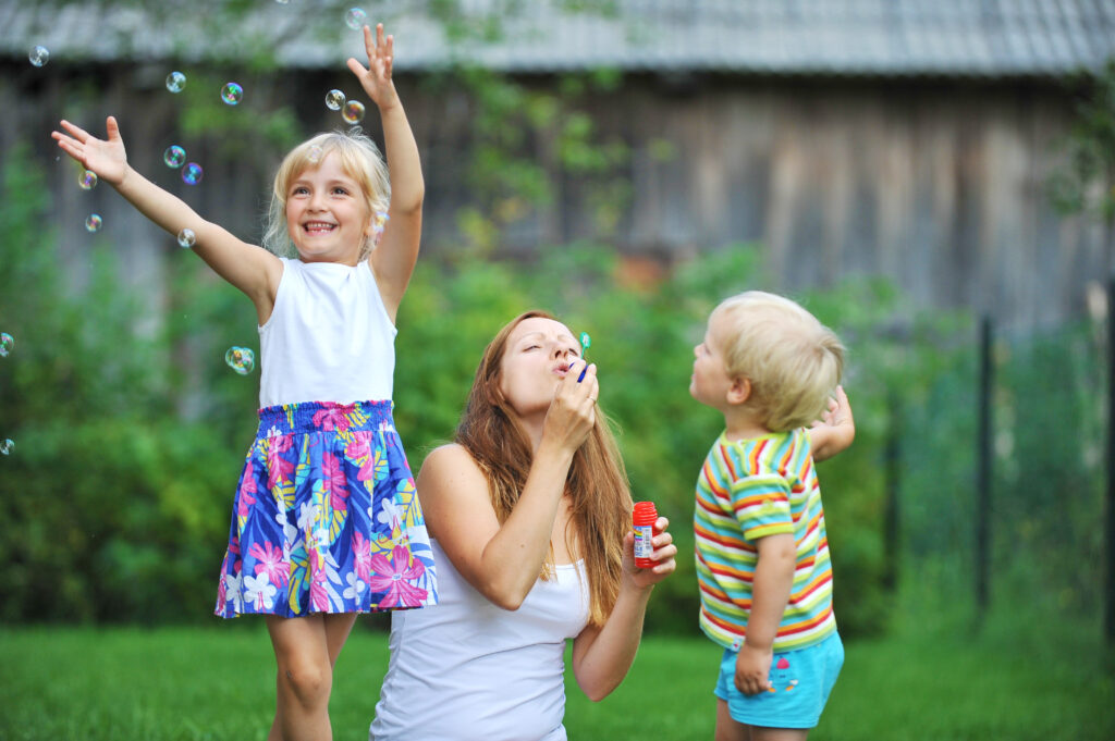 A woman and two children blowing bubbles in the yard.