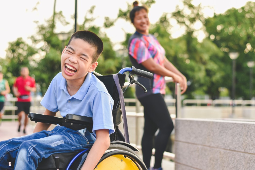 A man and boy in a wheelchair smiling for the camera.