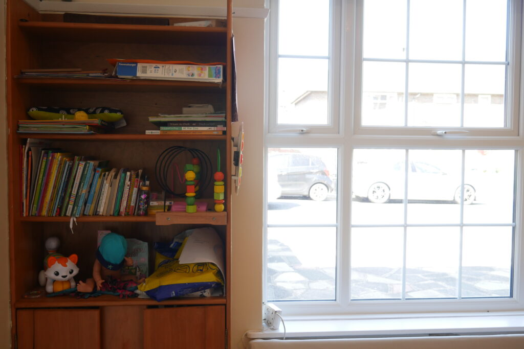 A bookshelf with books and toys in front of a window.