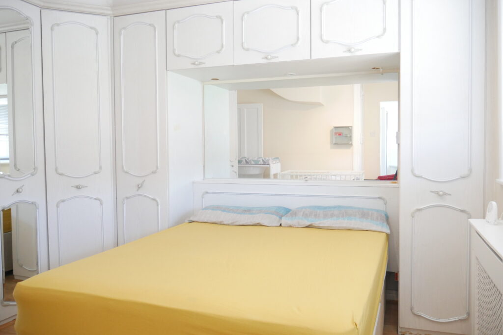 A bed room with a yellow bedspread and white cabinets