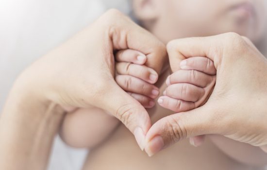 A baby is holding its mother 's hands in the shape of heart.